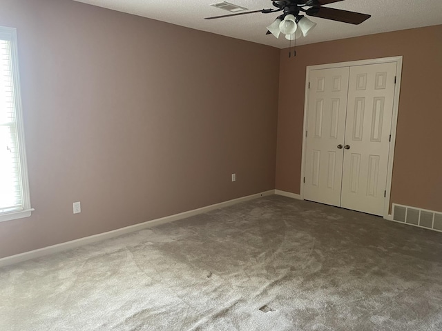 unfurnished bedroom with carpet flooring, ceiling fan, a textured ceiling, and a closet