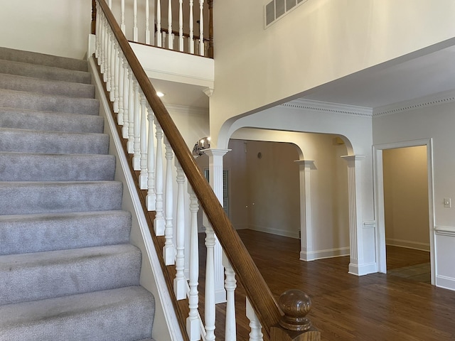 stairs with decorative columns, crown molding, and hardwood / wood-style floors