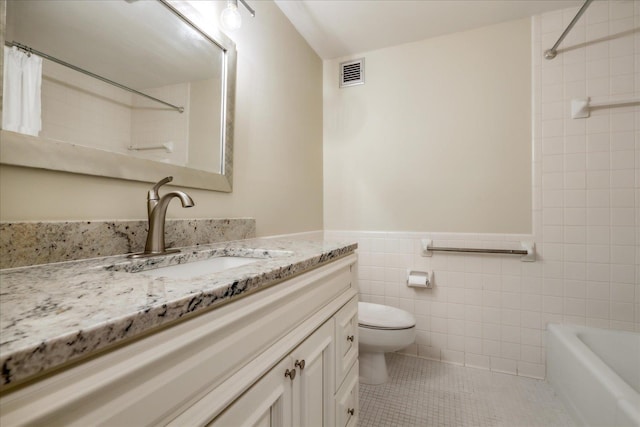 full bathroom with vanity, tile patterned floors, tiled shower / bath combo, toilet, and tile walls