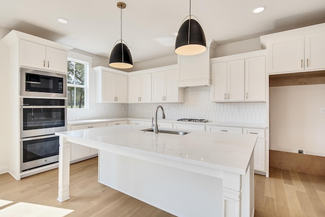 kitchen featuring black microwave, stainless steel double oven, a sink, gas stovetop, and light wood finished floors