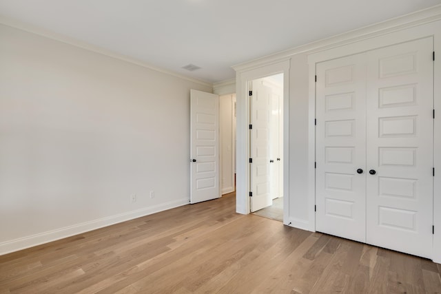 unfurnished bedroom with light wood-style flooring, visible vents, baseboards, a closet, and crown molding