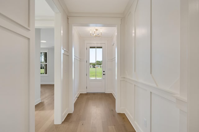 doorway with a chandelier, light wood finished floors, crown molding, and a decorative wall