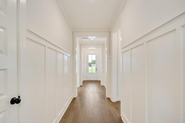 hallway with ornamental molding, a decorative wall, and wood finished floors