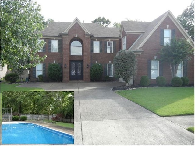 view of front of house featuring a front yard, a fenced in pool, concrete driveway, french doors, and brick siding