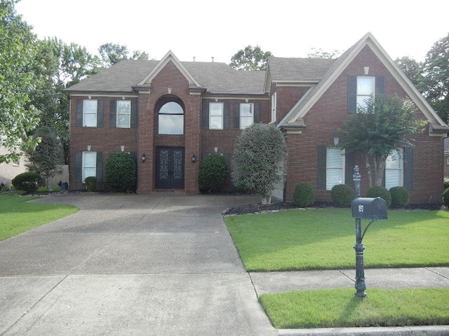 view of front facade with brick siding, french doors, concrete driveway, and a front yard