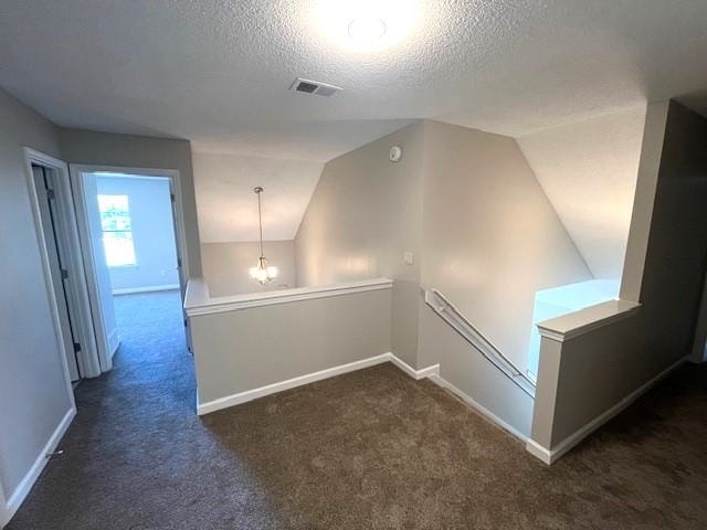 hall with lofted ceiling, a textured ceiling, and dark colored carpet