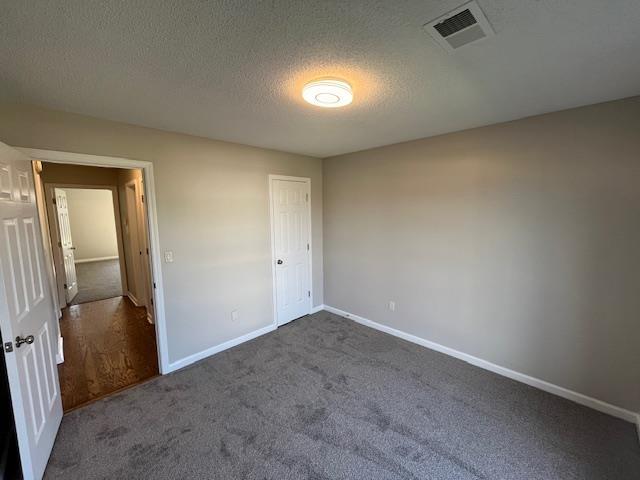 unfurnished bedroom with dark carpet, a textured ceiling, and a closet