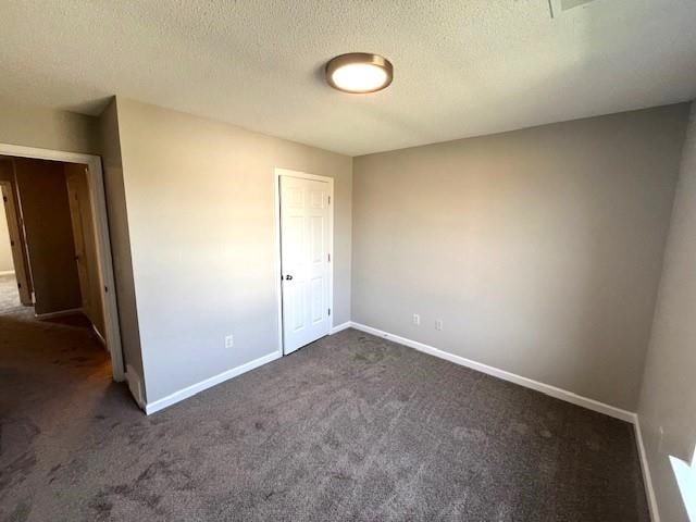 unfurnished bedroom featuring a textured ceiling and dark carpet