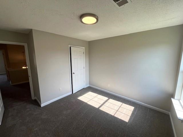 unfurnished bedroom featuring dark carpet and a textured ceiling