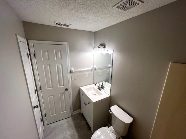 bathroom featuring vanity, toilet, concrete flooring, and a textured ceiling