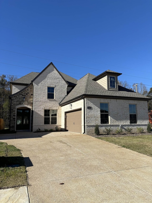 french provincial home with roof with shingles, an attached garage, concrete driveway, french doors, and brick siding