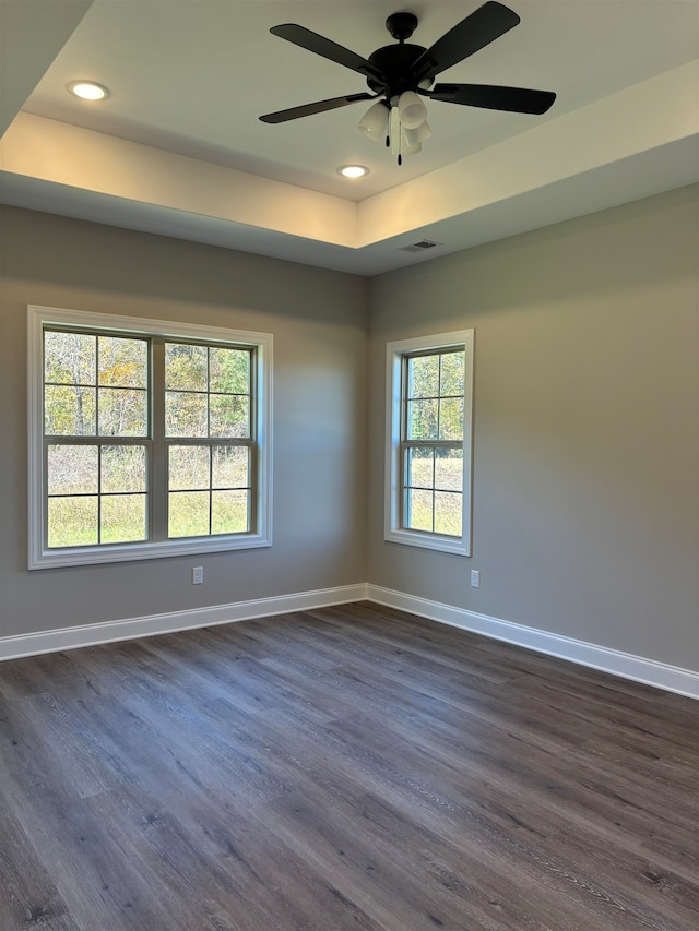 empty room with dark hardwood / wood-style floors, ceiling fan, and a tray ceiling