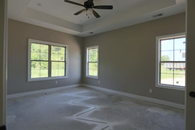 empty room with a tray ceiling, plenty of natural light, and ceiling fan