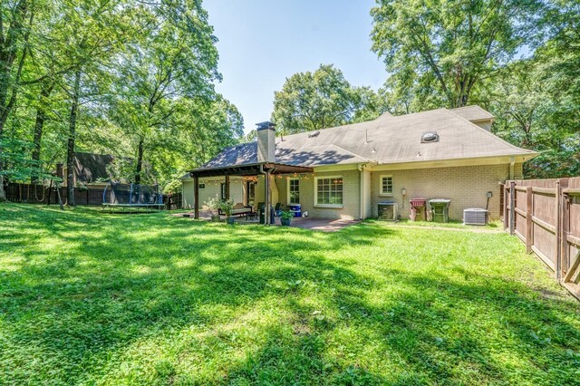 back of property featuring a trampoline, brick siding, a yard, and central AC unit