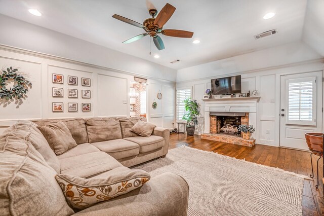 living room featuring a fireplace, visible vents, a decorative wall, and dark wood finished floors