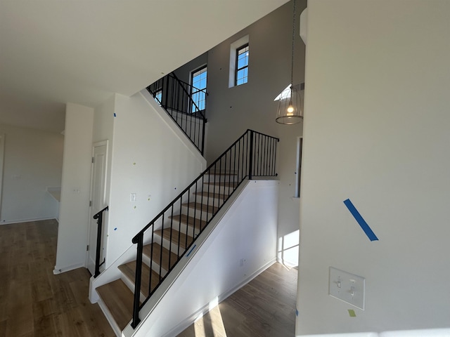 stairway with wood-type flooring, a towering ceiling, and a chandelier