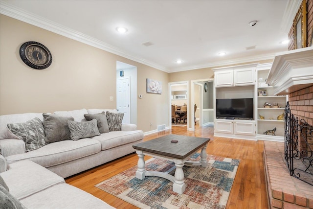 living room with built in shelves, crown molding, light hardwood / wood-style flooring, and a fireplace