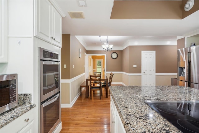 kitchen with an inviting chandelier, white cabinets, ornamental molding, light stone counters, and stainless steel appliances