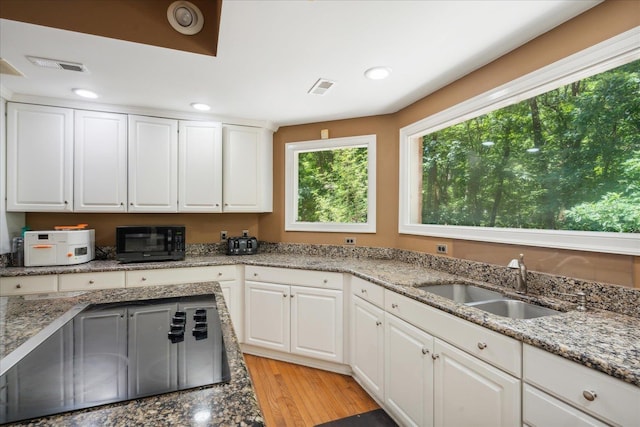 kitchen with black appliances, sink, light stone countertops, light hardwood / wood-style floors, and white cabinetry