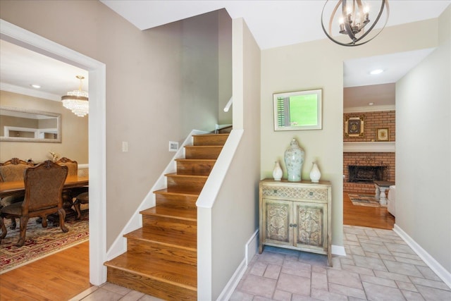 stairs with a brick fireplace, wood-type flooring, ornamental molding, and an inviting chandelier