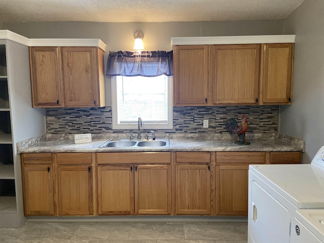 kitchen featuring a textured ceiling, decorative backsplash, washing machine and dryer, and sink