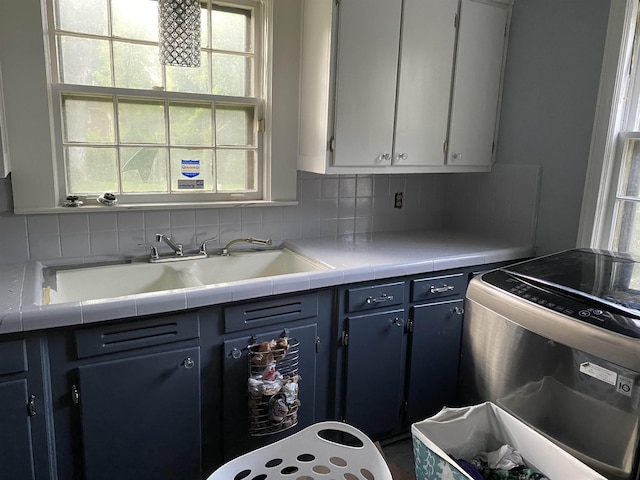 kitchen with stove, a sink, light countertops, blue cabinetry, and tasteful backsplash