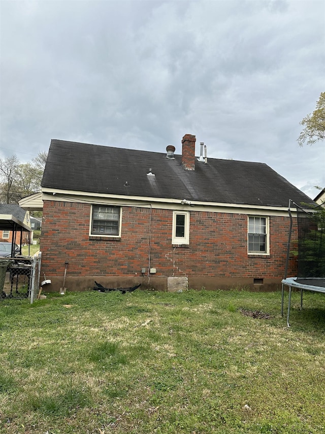 rear view of property with a trampoline, crawl space, brick siding, and a yard