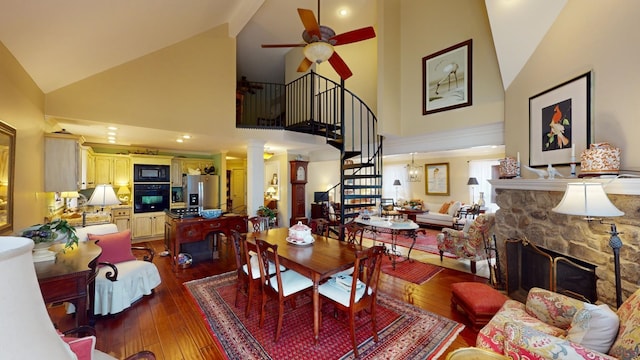 dining space featuring hardwood / wood-style flooring, ceiling fan, a fireplace, and high vaulted ceiling