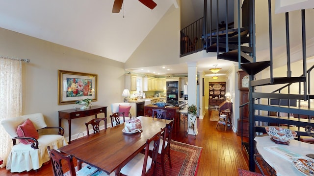 dining space featuring decorative columns, ceiling fan, sink, wood-type flooring, and high vaulted ceiling