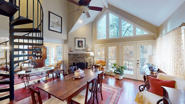 dining room featuring hardwood / wood-style flooring, a stone fireplace, high vaulted ceiling, and french doors