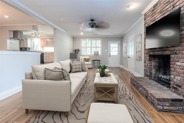 living room with a brick fireplace, ornamental molding, light hardwood / wood-style floors, and a healthy amount of sunlight