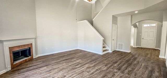 unfurnished living room with dark wood-type flooring, high vaulted ceiling, and a tiled fireplace