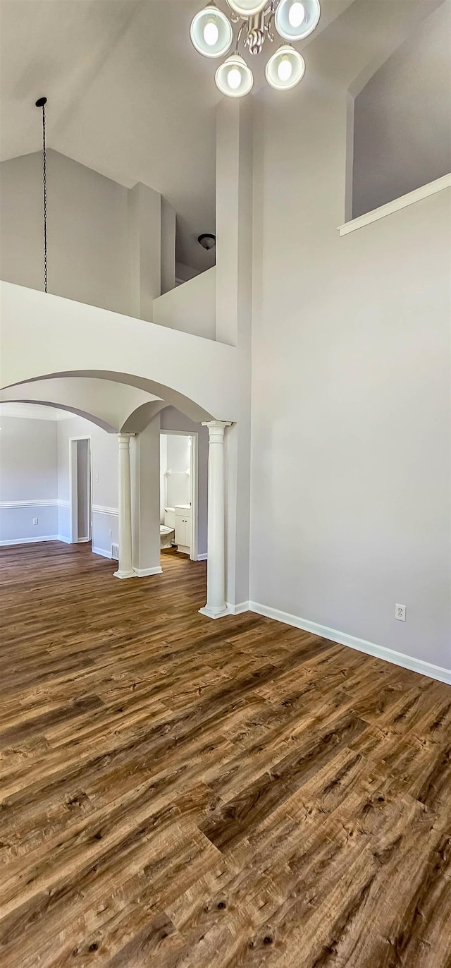 unfurnished living room with dark hardwood / wood-style flooring, a towering ceiling, and an inviting chandelier