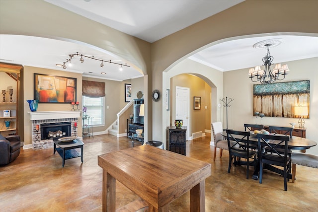 dining area with rail lighting, an inviting chandelier, concrete floors, a fireplace, and ornamental molding