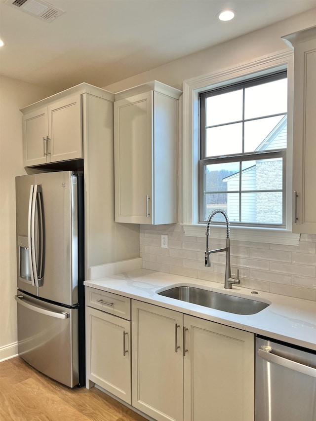 kitchen featuring white cabinets, sink, decorative backsplash, light wood-type flooring, and appliances with stainless steel finishes