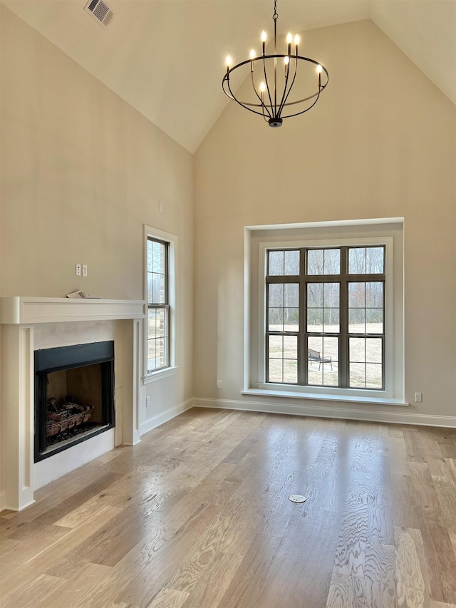 unfurnished living room featuring a chandelier, high vaulted ceiling, and light hardwood / wood-style floors