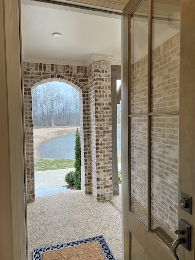 entryway with a water view, crown molding, and brick wall