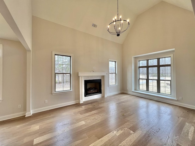 unfurnished living room featuring light hardwood / wood-style floors, high vaulted ceiling, and an inviting chandelier