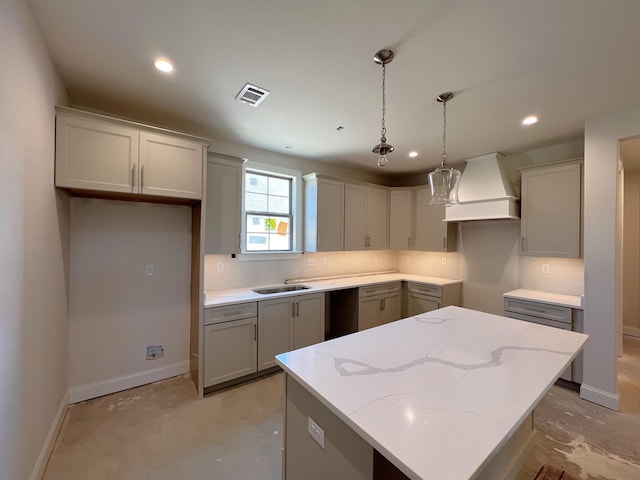 kitchen with light stone counters, a center island, hanging light fixtures, and custom range hood