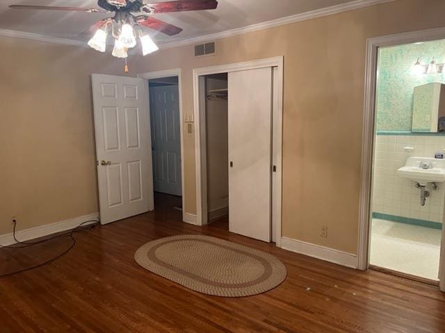 unfurnished bedroom with ensuite bath, ceiling fan, crown molding, wood-type flooring, and a closet