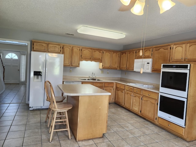 kitchen featuring sink, light tile patterned flooring, white appliances, a breakfast bar area, and a kitchen island