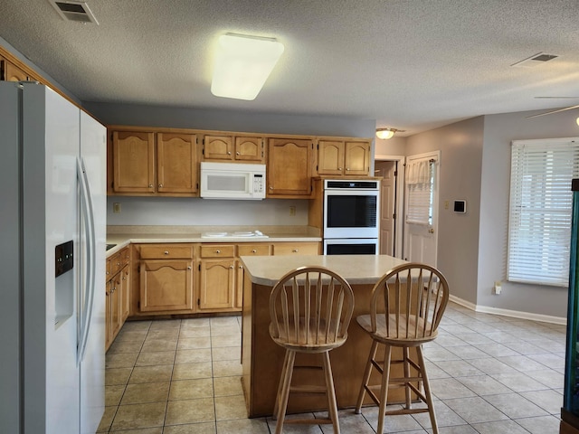 kitchen with a kitchen breakfast bar, white appliances, ceiling fan, light tile patterned floors, and a center island