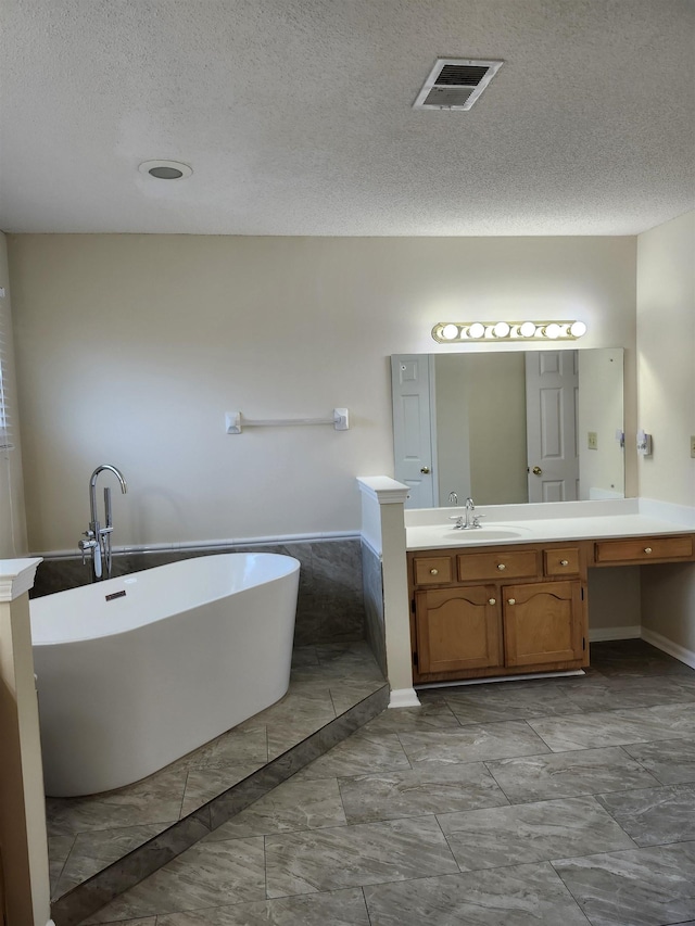 bathroom with a tub to relax in, vanity, and a textured ceiling