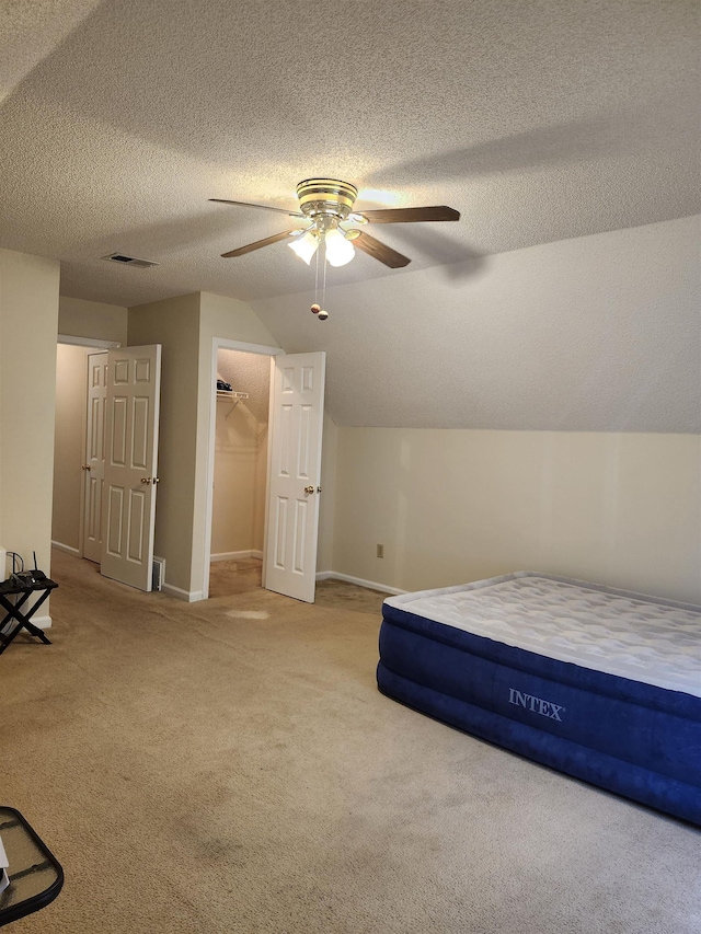 unfurnished bedroom featuring lofted ceiling, light carpet, a walk in closet, ceiling fan, and a closet