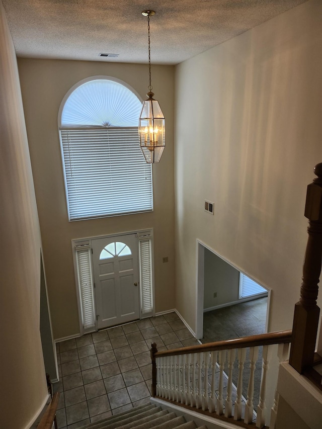 tiled entrance foyer with a chandelier, a towering ceiling, and a textured ceiling