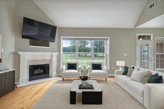 living room with vaulted ceiling, light hardwood / wood-style flooring, and a tiled fireplace