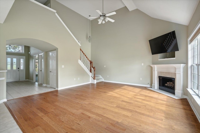 unfurnished living room with a tile fireplace, ceiling fan, high vaulted ceiling, and light hardwood / wood-style floors