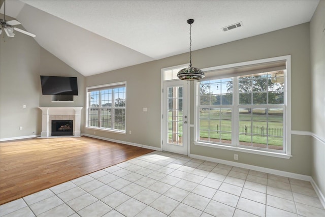 unfurnished living room featuring lofted ceiling, light tile patterned floors, a fireplace, and ceiling fan with notable chandelier