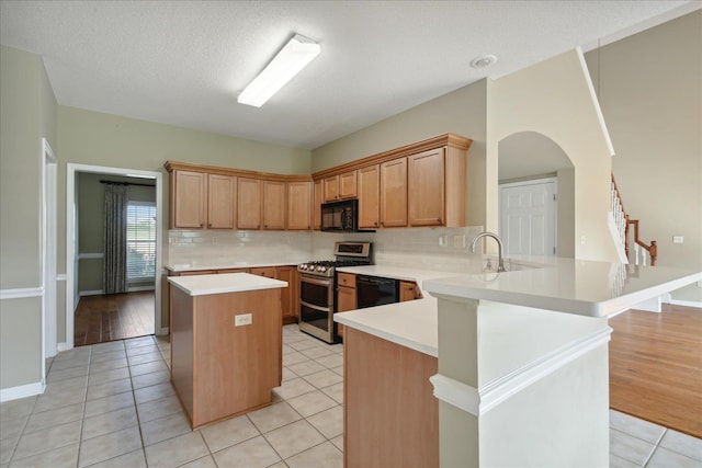 kitchen featuring black appliances, light tile patterned floors, a textured ceiling, a kitchen island, and kitchen peninsula