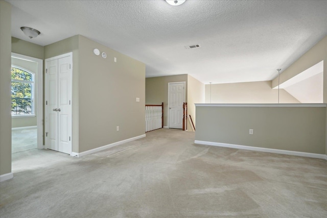 empty room featuring vaulted ceiling, light carpet, and a textured ceiling